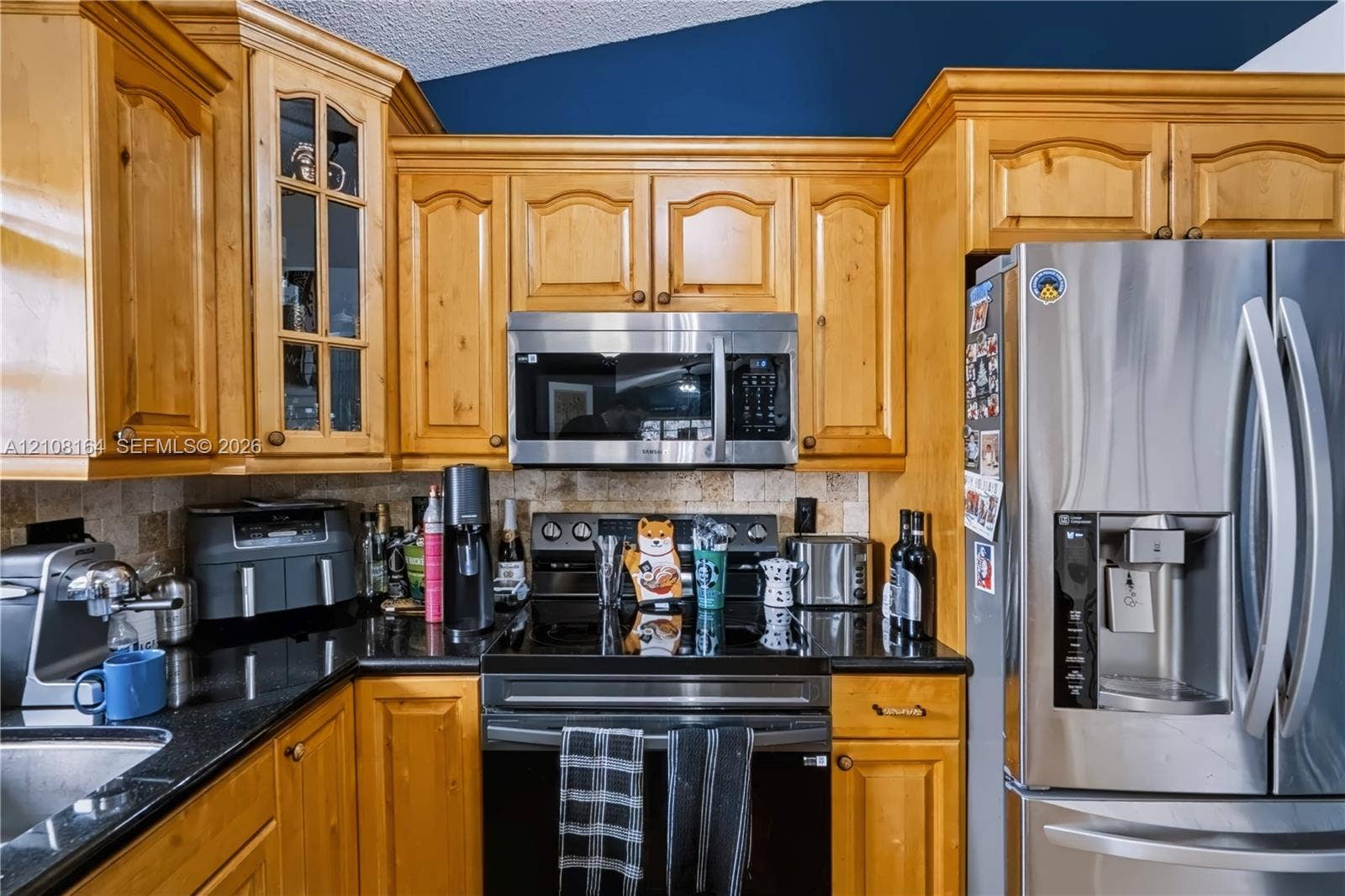 3983 NW 122nd Terrace, Sunrise, FL 33323 Kitchen featuring natural wood cabinetry, polished black stone countertops, stone tile backsplash, and stainless steel appliances including a built-in microwave and refrigerator