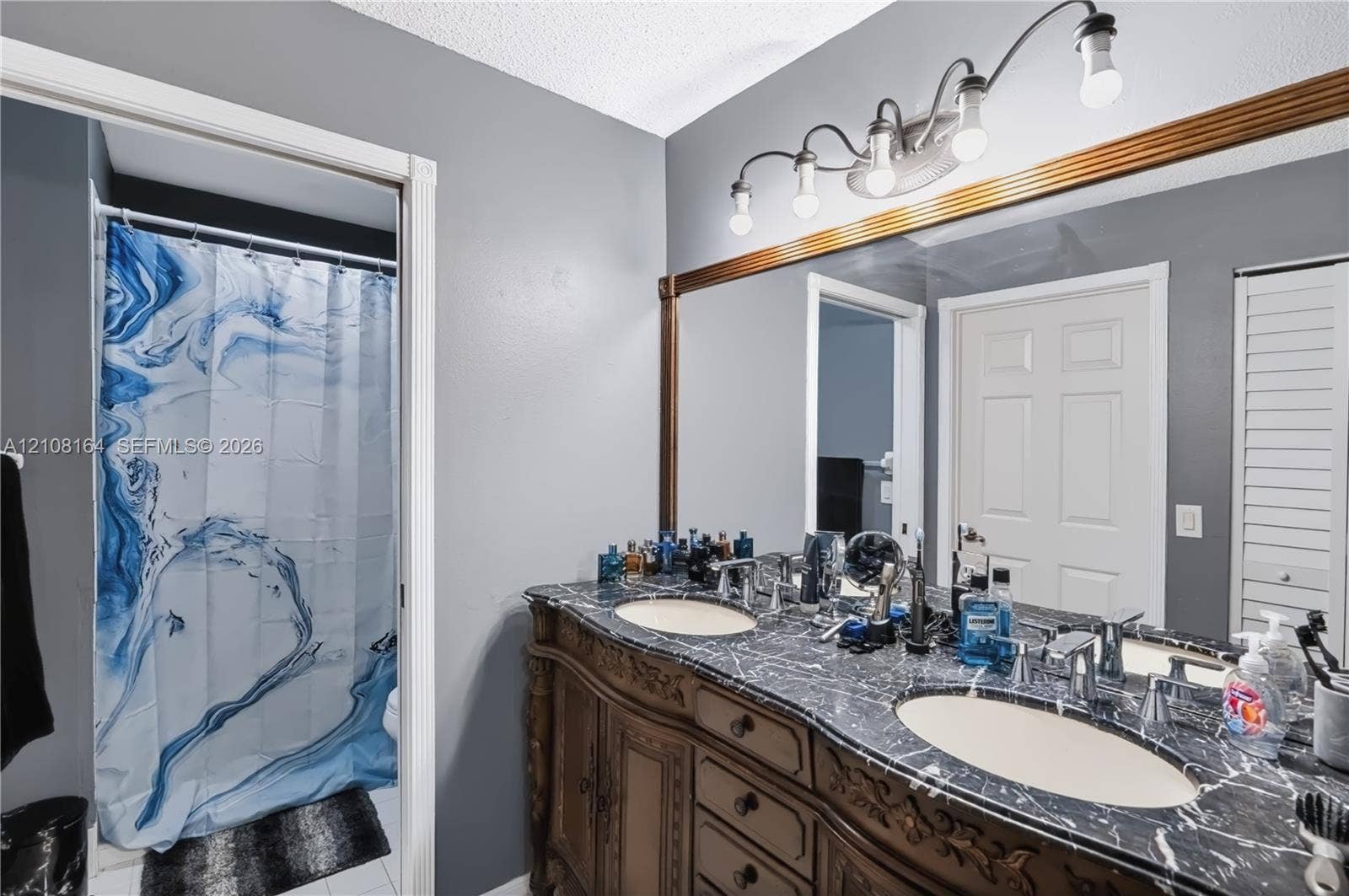3983 NW 122nd Terrace, Sunrise, FL 33323 Custom wood cabinetry with ornate detailing, dual under-mount sinks, stone-finish countertops, full-width wall mirror with wood trim, and multi-light vanity fixture