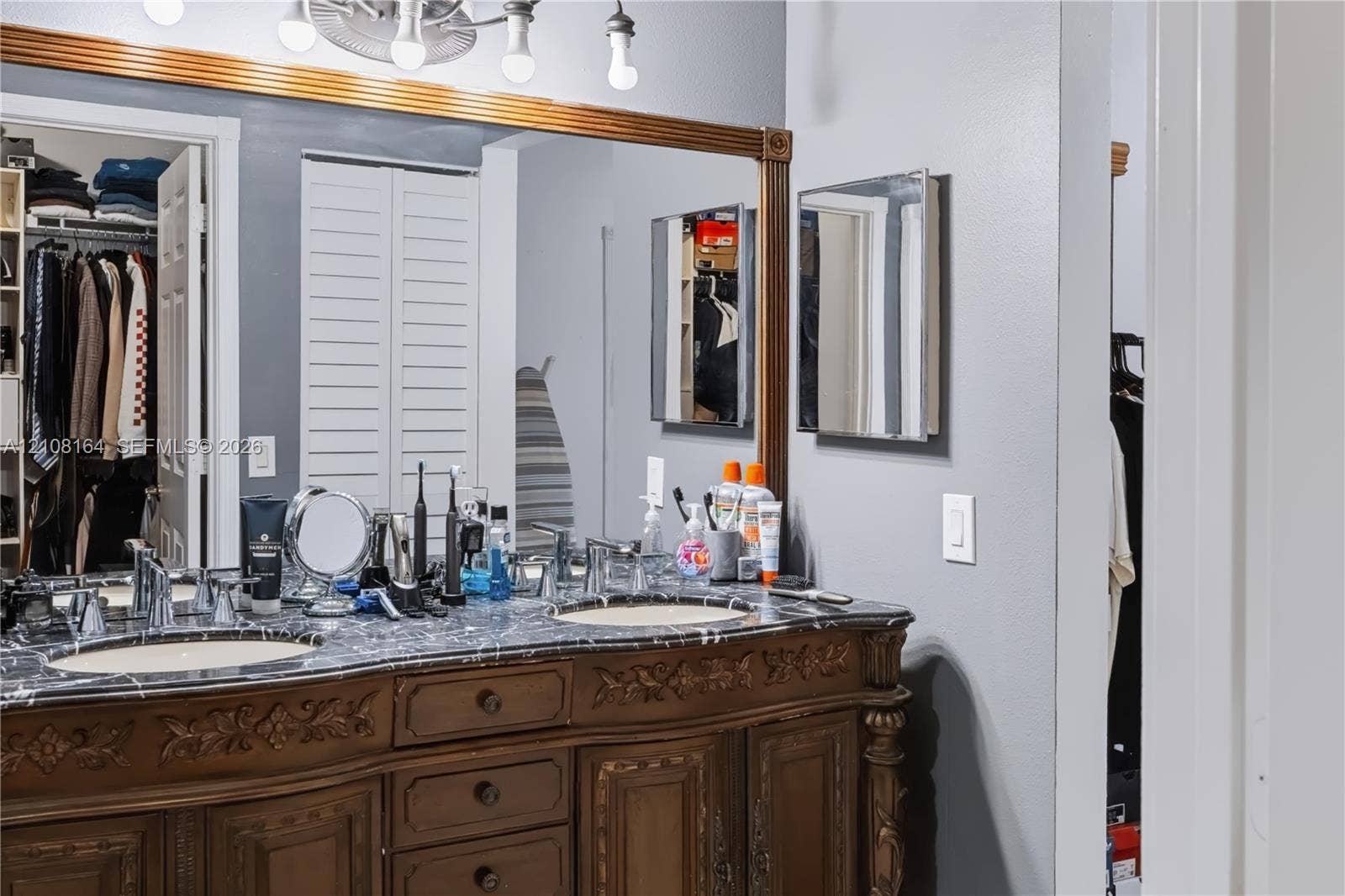 3983 NW 122nd Terrace, Sunrise, FL 33323 Double vanity featuring a stone countertop, dual undermount sinks, intricate wood cabinetry with carved detailing, and a wall-to-wall framed mirror
