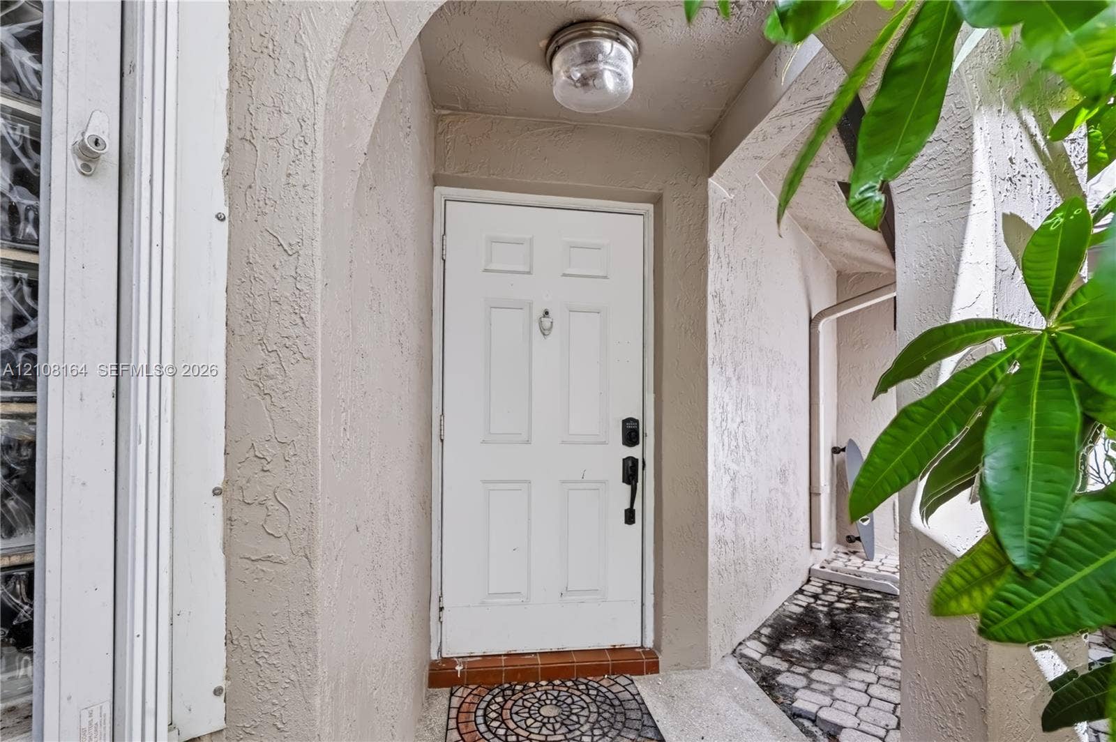 3983 NW 122nd Terrace, Sunrise, FL 33323 Covered entryway featuring a recessed arched alcove, a multi-panel white entry door with a brass-finish knocker, and a decorative circular mosaic tile inlay at the threshold