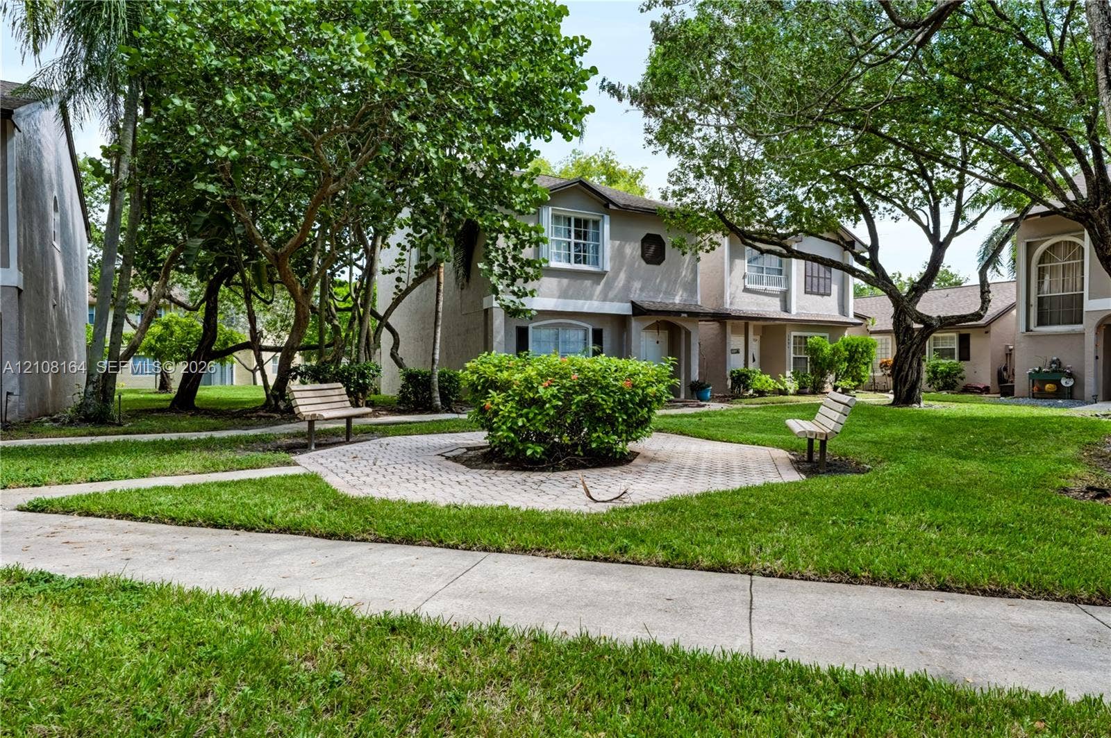 3983 NW 122nd Terrace, Sunrise, FL 33323 Exterior grounds featuring paved walkways, a central stone-paver hardscape, mature landscaping, and outdoor seating