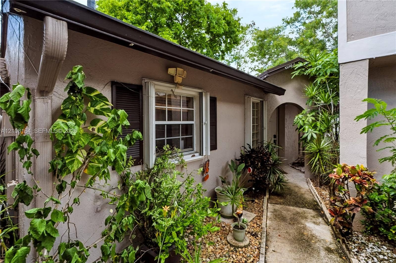 3983 NW 122nd Terrace, Sunrise, FL 33323 Stucco exterior featuring dual-pane windows with dark shutters, a covered arched entryway, and a stone-lined walkway