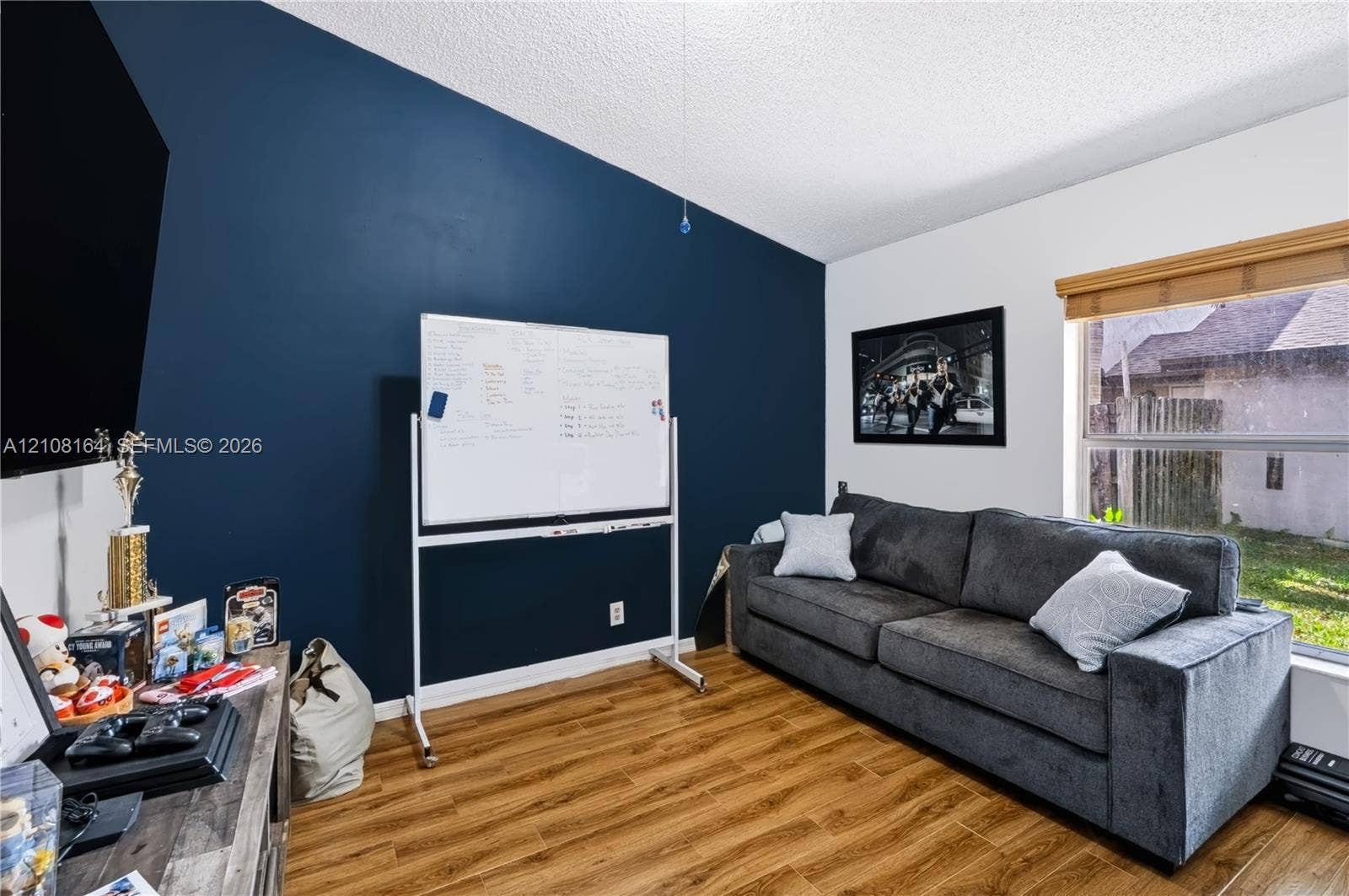 3983 NW 122nd Terrace, Sunrise, FL 33323 Room featuring wood-finish flooring, a bold navy accent wall, and a horizontal window with wood-slat blinds