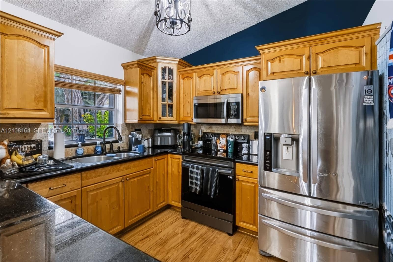 3983 NW 122nd Terrace, Sunrise, FL 33323 Kitchen featuring wood cabinetry, stone countertops, stainless steel appliances, a vaulted ceiling with a decorative pendant light, and wood-finish flooring