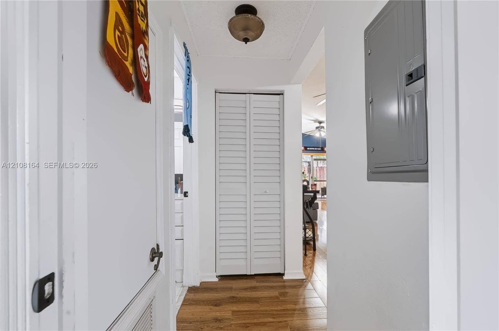 3983 NW 122nd Terrace, Sunrise, FL 33323 Hallway featuring wood-finish flooring, white louvered bifold closet doors, a neutral-tone flush-mount ceiling light fixture, and a wall-mounted electrical panel