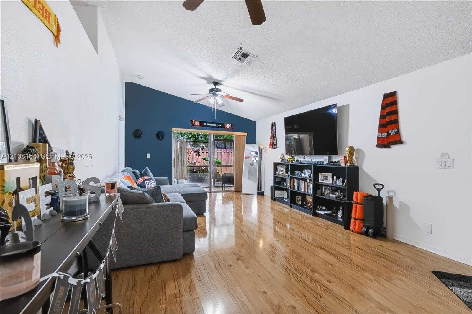 3983 NW 122nd Terrace, Sunrise, FL 33323 Living room featuring vaulted ceilings, wood-finish flooring, two ceiling fans, and a sliding glass door