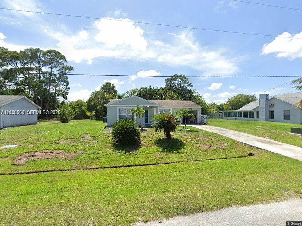 Single-story residence featuring a light-toned exterior, concrete driveway, attached garage, and mature landscaping