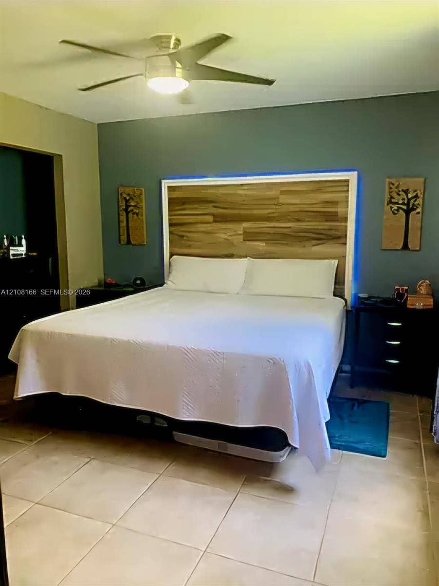 Room featuring large-format tile flooring, a multi-blade ceiling fan with integrated lighting, and a custom wood-finish headboard accent wall with perimeter backlighting