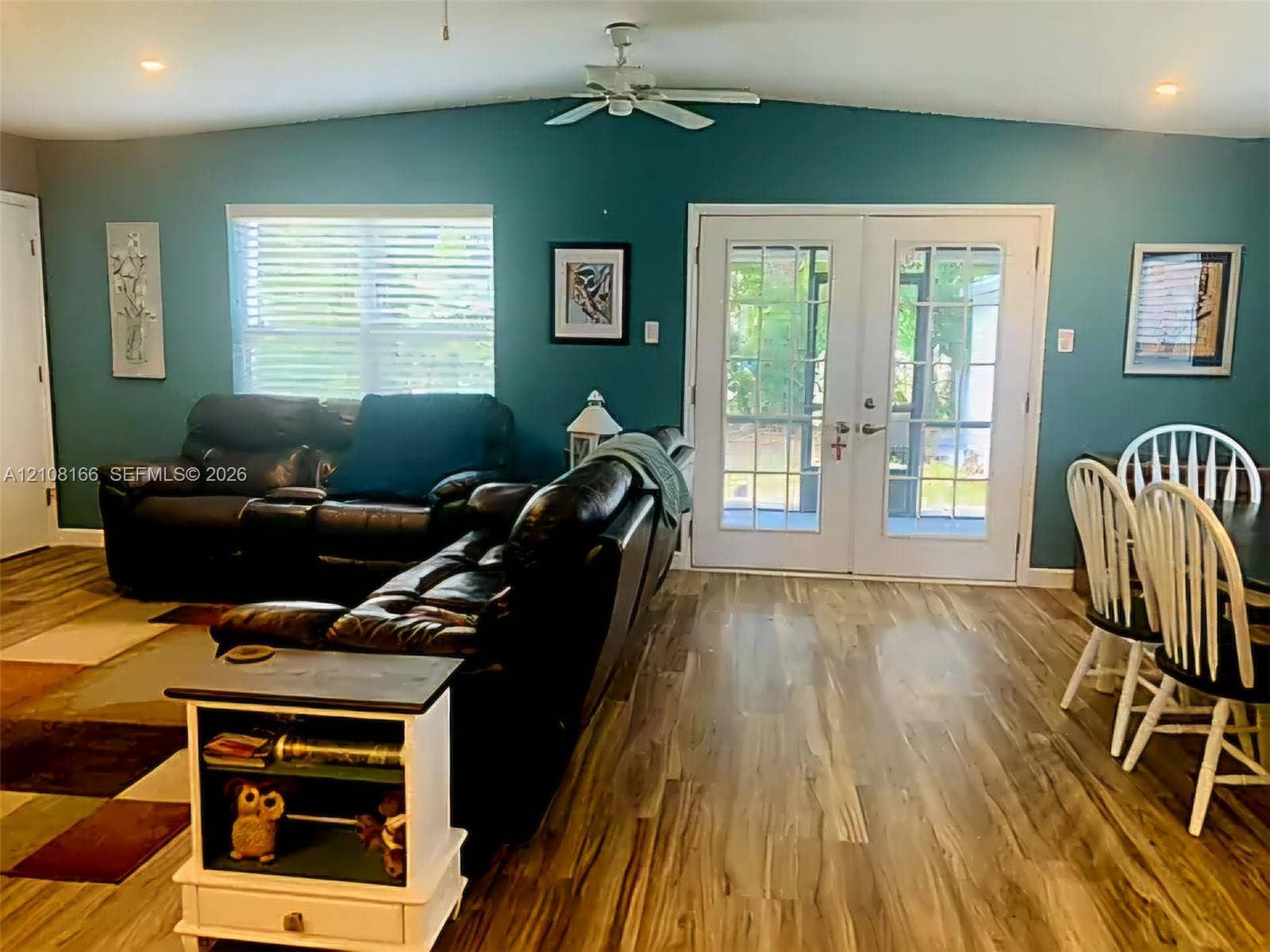 Vaulted ceiling with integrated paddle fan, wood-finish flooring, and glass-paneled double doors providing outdoor access