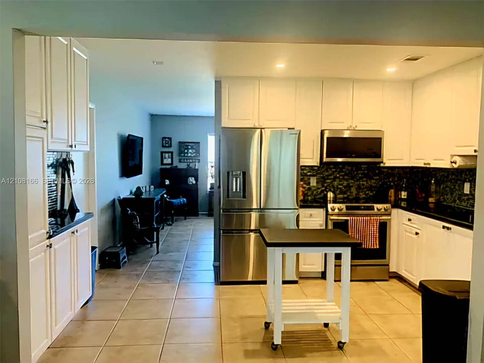 Kitchen featuring white shaker-style cabinetry, dark stone countertops, tile flooring, and stainless steel appliances including a refrigerator and over-the-range microwave