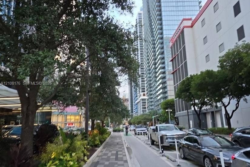 Urban streetscape featuring patterned paver walkways, mature canopy trees, and high-rise glass-faade architecture