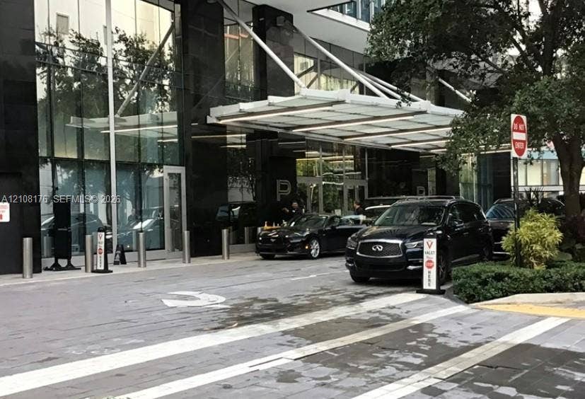 Contemporary building exterior featuring a polished black stone facade, expansive floor-to-ceiling glass paneling, and a cantilevered architectural canopy over a paved motor court