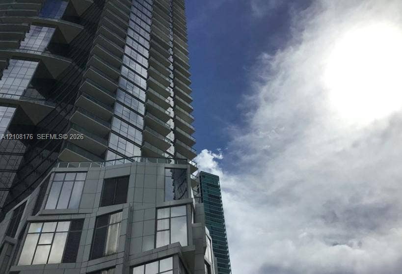 High-rise tower exterior featuring a glass and metal facade, geometric structural articulation, and wrap-around balconies with glass railings