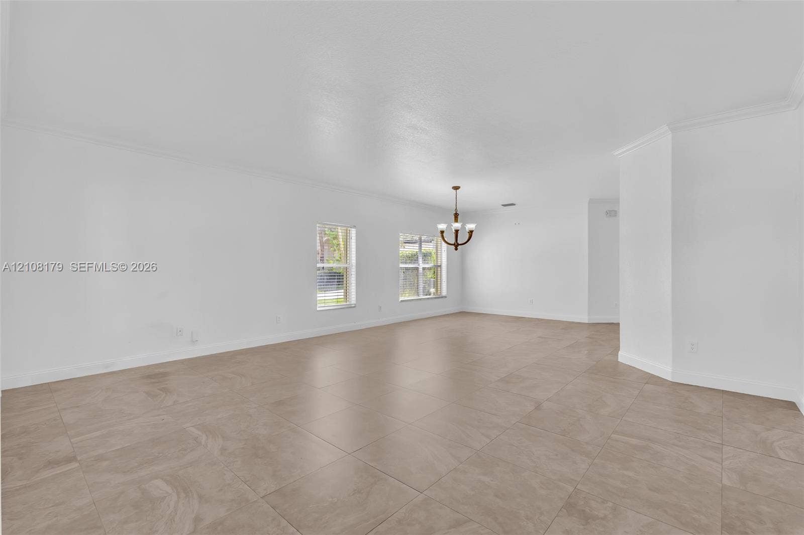 15854 SW 14th Court, Pembroke Pines, Pembroke Pines, FL 33027 Open-concept interior featuring large-format tile flooring, recessed crown molding, dual windows, and a multi-arm chandelier