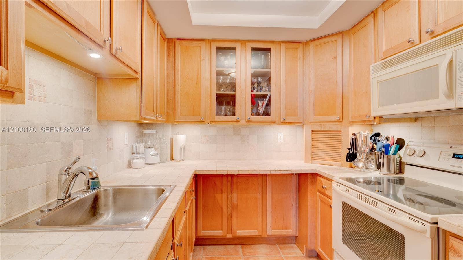 2457 Collins Avenue, #1501, Miami Beach, FL 33140 Kitchen featuring natural wood cabinetry, light-toned tile countertops, tiled backsplash, recessed ceiling lighting, and integrated over-the-range microwave