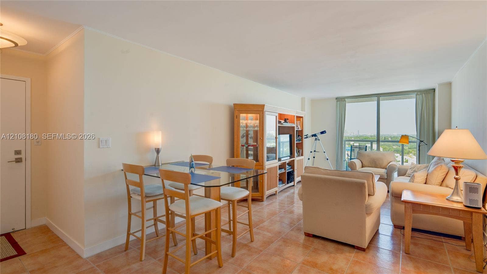 2457 Collins Avenue, #1501, Miami Beach, FL 33140 Open-concept interior featuring neutral wall tones, ceramic tile flooring, built-in wooden cabinetry, and floor-to-ceiling glass sliding doors leading to a private balcony