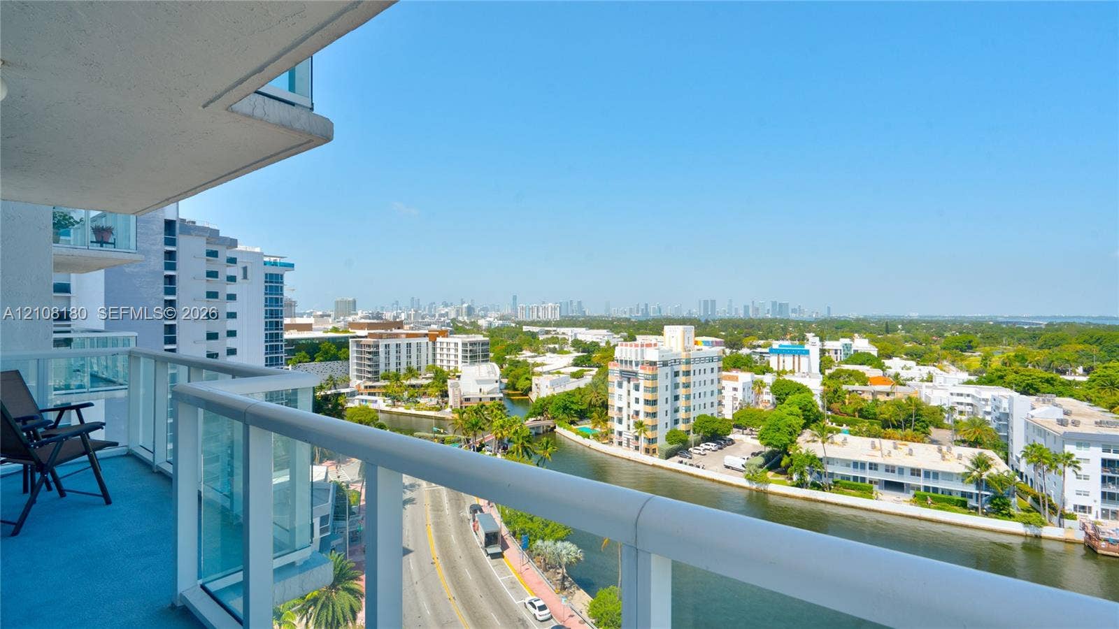 2457 Collins Avenue, #1501, Miami Beach, FL 33140 Covered balcony with a white metal railing and glass panel inserts, providing an exterior perspective of the canal and urban skyline