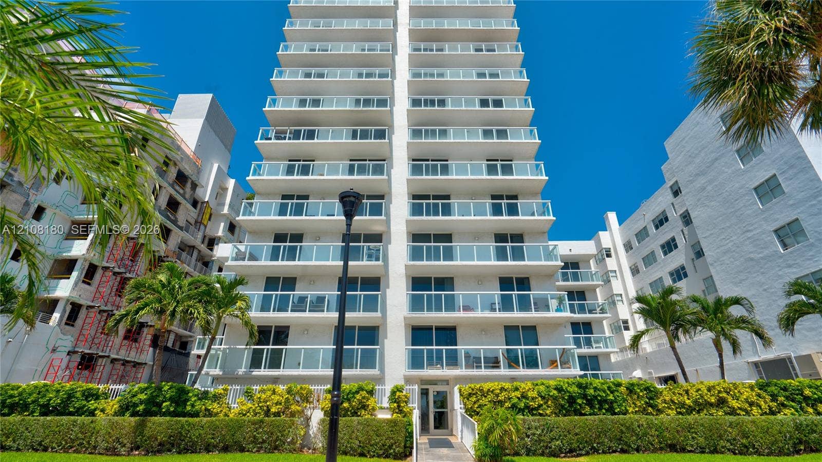 2457 Collins Avenue, #1501, Miami Beach, FL 33140 Multi-story high-rise exterior featuring stacked glass-railing balconies, floor-to-ceiling windows, white facade, and manicured landscaping