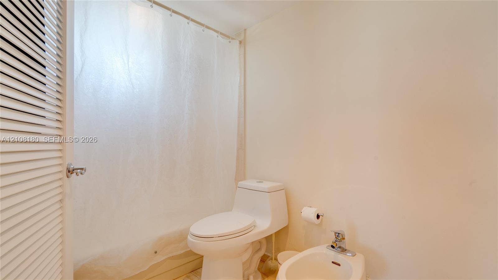 2457 Collins Avenue, #1501, Miami Beach, FL 33140 Bathroom featuring a white elongated toilet, porcelain bidet with chrome faucet, shower-tub combination with a curtain, and louvered closet door