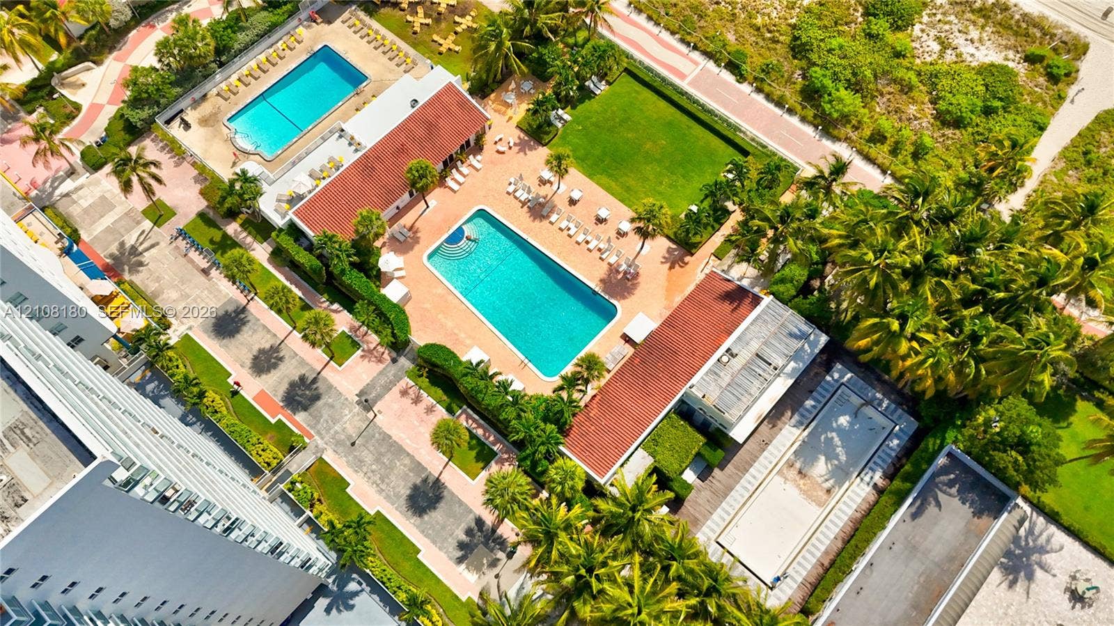 2457 Collins Avenue, #1501, Miami Beach, FL 33140 Aerial perspective of the grounds featuring two outdoor swimming pools, manicured lawn space, paved walkways, and mature palm trees