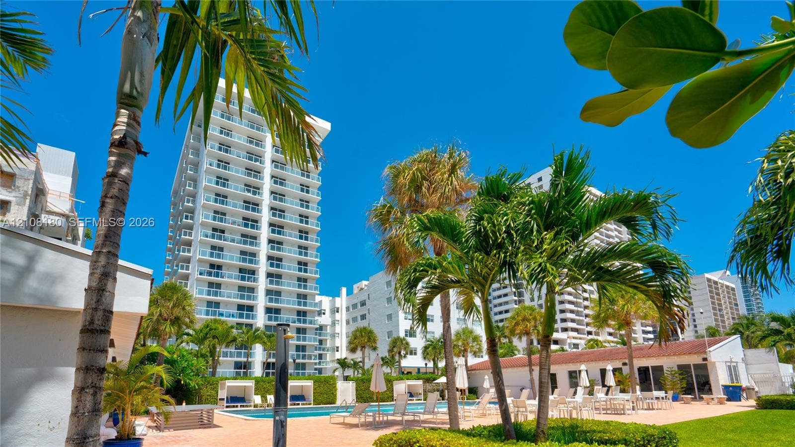 2457 Collins Avenue, #1501, Miami Beach, FL 33140 High-rise residential exterior featuring glass-railed balconies, exterior swimming pool, hardscaped patio area, mature palm trees, and manicured landscaping