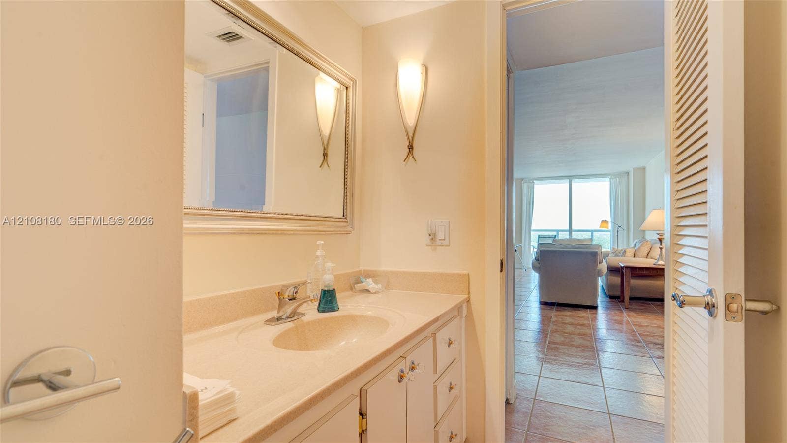 2457 Collins Avenue, #1501, Miami Beach, FL 33140 Vanity with integrated sink and countertop, framed wall mirror, dual wall-mounted sconces, and louvered-style closet door