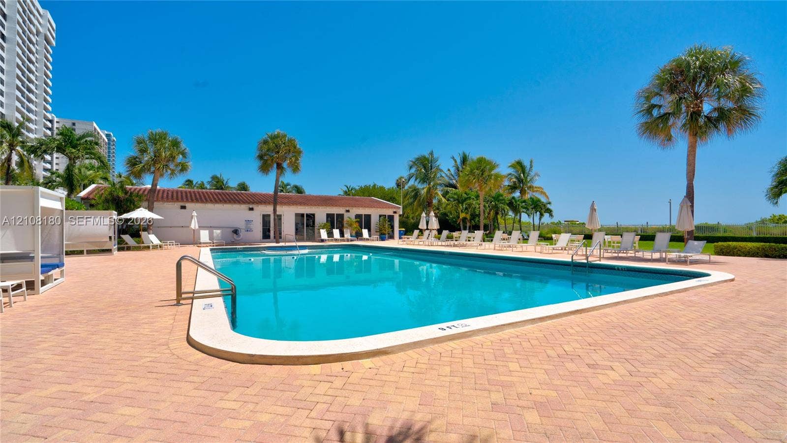 2457 Collins Avenue, #1501, Miami Beach, FL 33140 In-ground swimming pool surrounded by a paver deck, palm trees, and a low-profile clubhouse with a clay tile roof