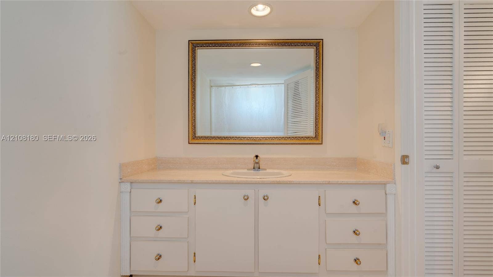 2457 Collins Avenue, #1501, Miami Beach, FL 33140 Vanity featuring a stone countertop, integrated sink, white cabinetry with metallic hardware, and a framed wall-mounted mirror