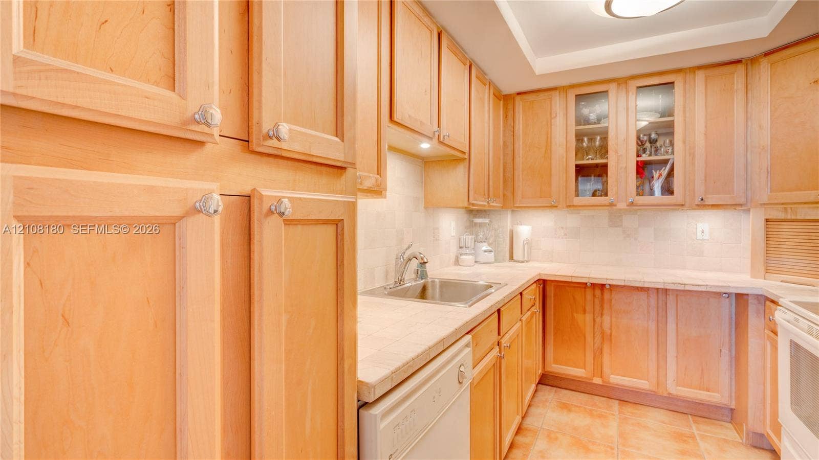 2457 Collins Avenue, #1501, Miami Beach, FL 33140 Kitchen featuring natural wood cabinetry, tile countertops, glass-front upper cabinet doors, under-cabinet lighting, and ceramic tile flooring