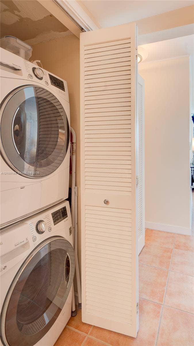 2457 Collins Avenue, #1501, Miami Beach, FL 33140 Laundry area featuring stacked appliances enclosed by a white louvered bifold door and tile flooring