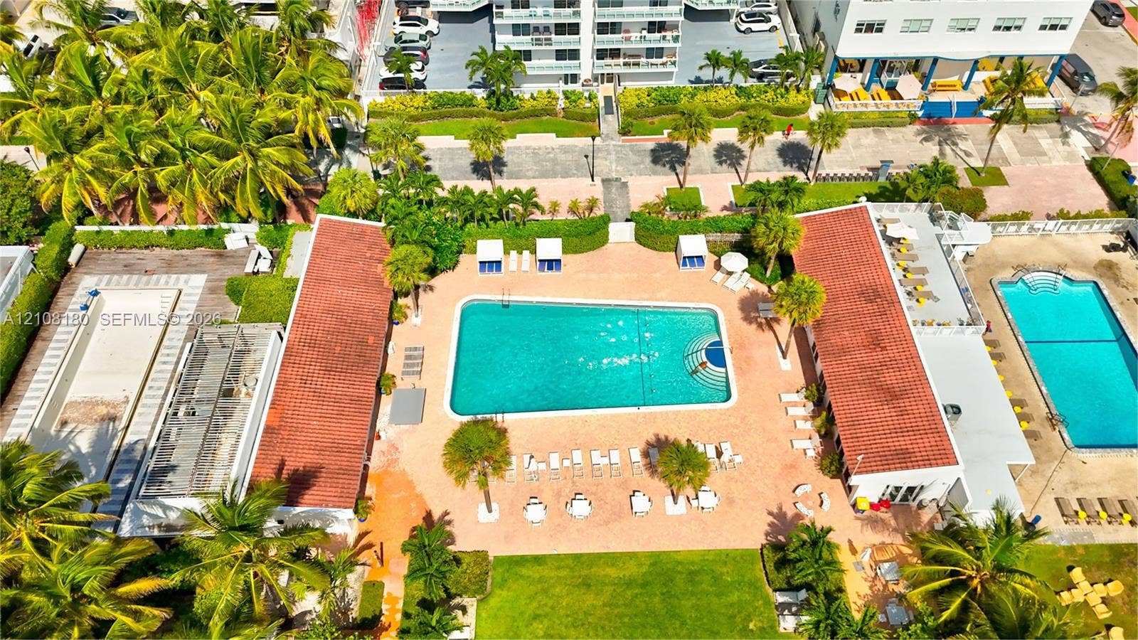 2457 Collins Avenue, #1501, Miami Beach, FL 33140 Aerial perspective of a multi-pool courtyard featuring terracotta-tiled roofs, manicured lawns, mature palm trees, and paved deck surfaces