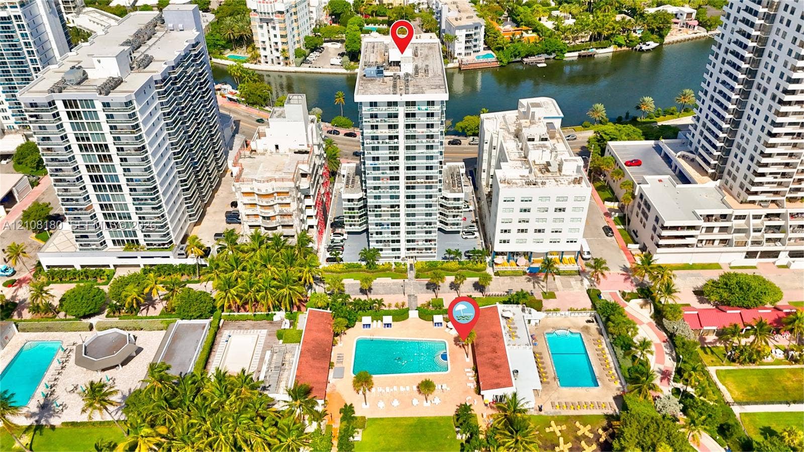 2457 Collins Avenue, #1501, Miami Beach, FL 33140 High-rise residential building featuring exterior balconies, a ground-level swimming pool, and tropical landscaping situated along a waterway