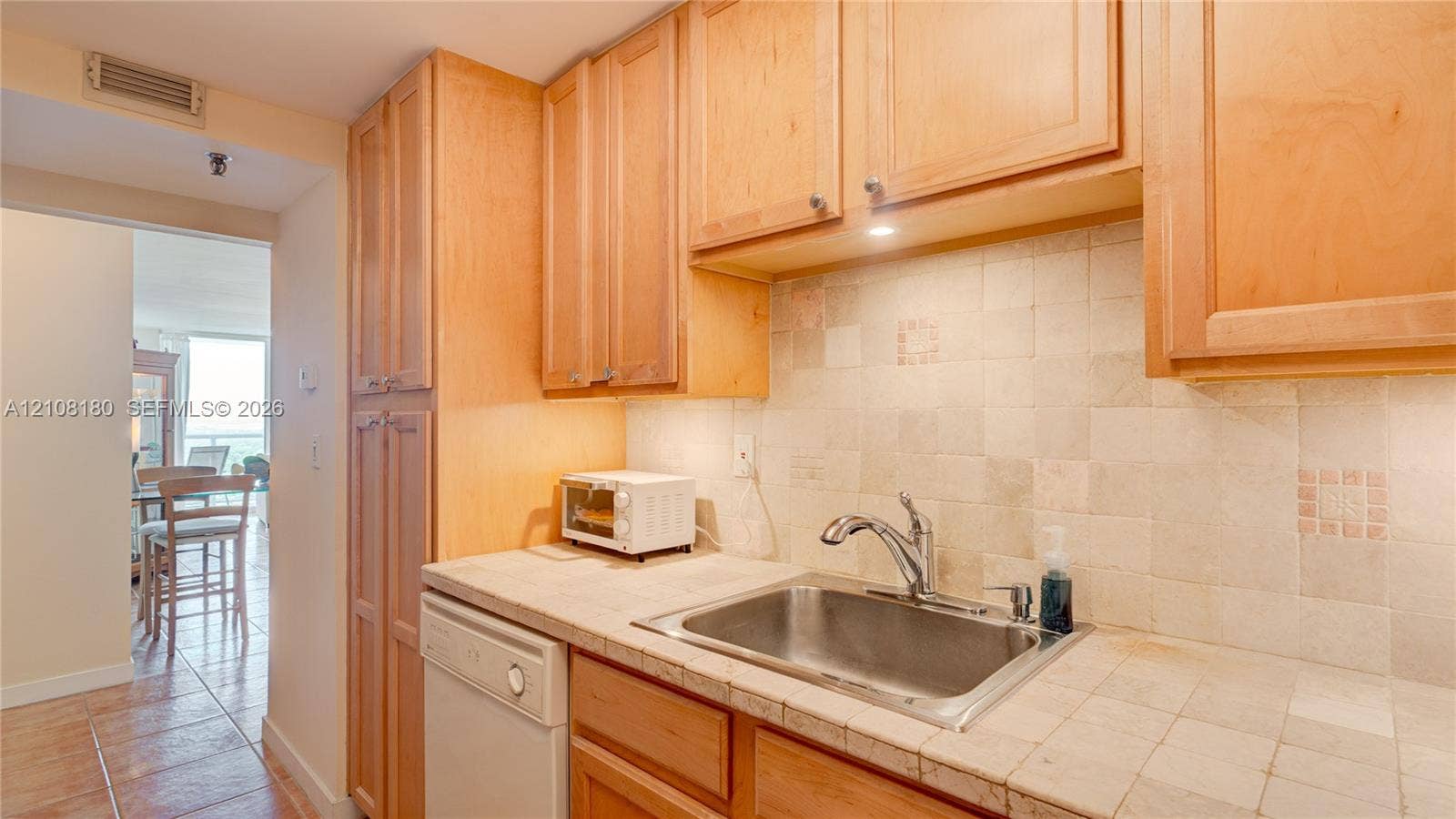 2457 Collins Avenue, #1501, Miami Beach, FL 33140 Kitchen featuring light-finish wood cabinetry, tile countertops, matching tile backsplash, and a stainless steel sink with a high-arch faucet