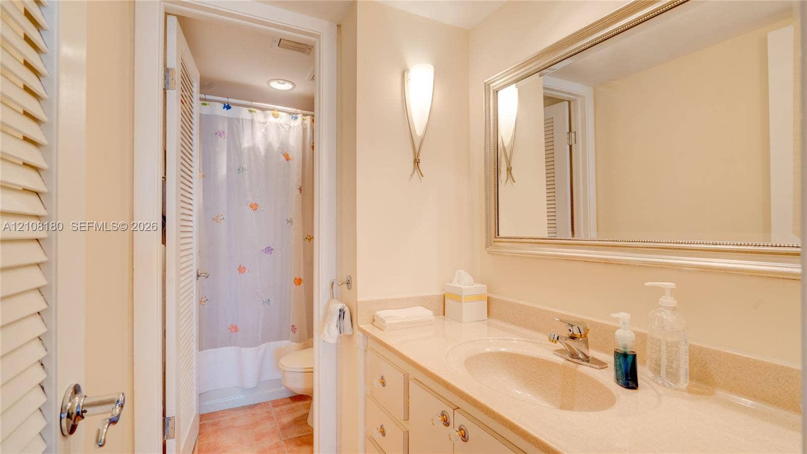 2457 Collins Avenue, #1501, Miami Beach, FL 33140 Bathroom vanity with a solid-surface countertop and integrated sink, complemented by a wide framed mirror, wall-mounted sconce lighting, and a separate water closet area featuring a tub-shower combination