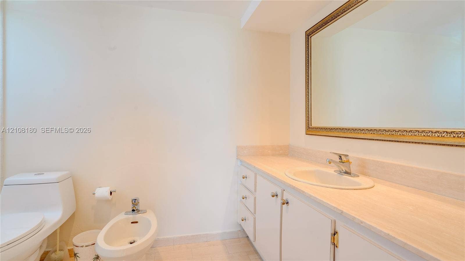 2457 Collins Avenue, #1501, Miami Beach, FL 33140 Bathroom featuring a neutral stone-finish countertop, white cabinetry with integrated storage, an oval undermount sink with a chrome faucet, a floor-mounted bidet, and a large wall-mounted mirror with a decorative frame