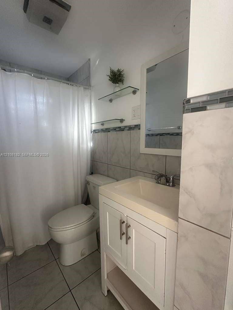 930 N 16th Avenue, #2, Hollywood, Hollywood, FL 33020 Bathroom featuring a white vanity cabinet with a stone-surface countertop, metal hardware, glass wall-mounted shelving, and tiled wall accents