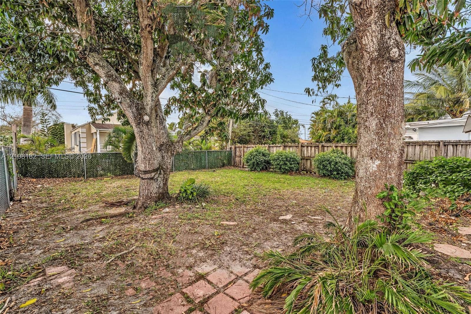 930 N 16th Avenue, #2, Hollywood, Hollywood, FL 33020 Backyard featuring mature trees, a wooden privacy fence, green lawn space, and a brick paver section