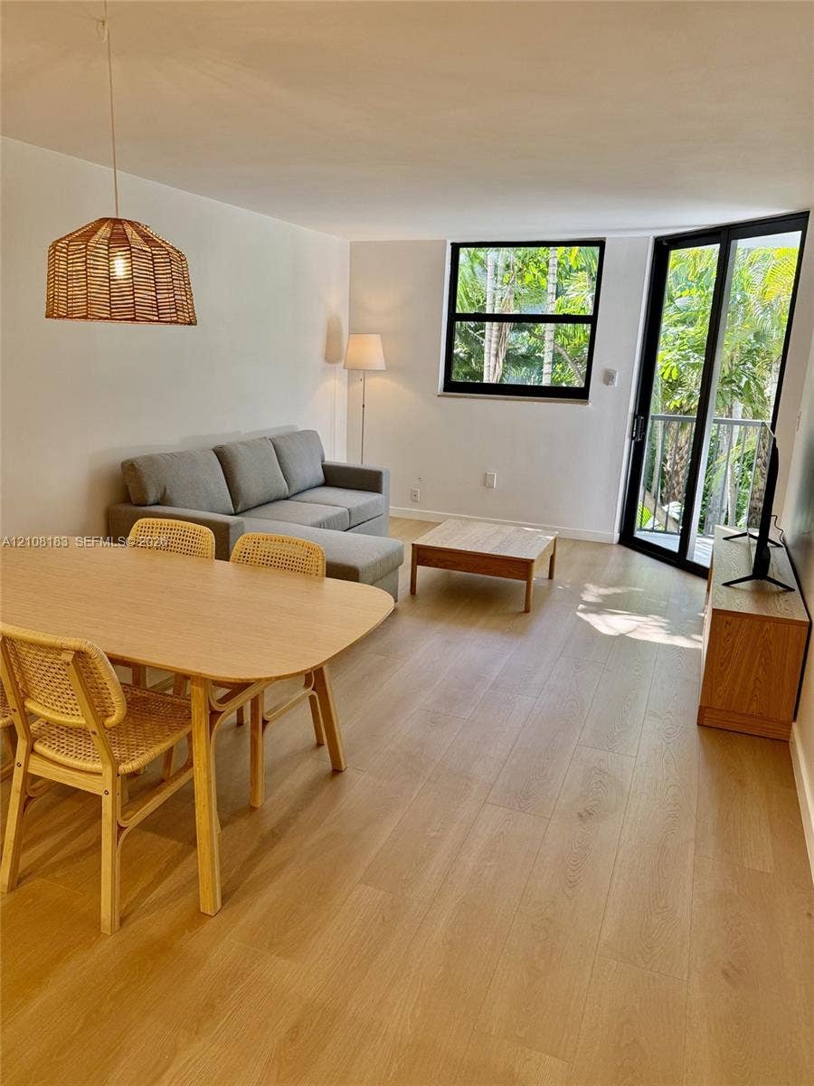 101 Ocean Lane Drive, #205, Key Biscayne, Key Biscayne, FL 33149 Open-concept living space featuring wood-finish flooring, a woven pendant light fixture, black-framed windows, and glass-paned doors opening to an outdoor balcony