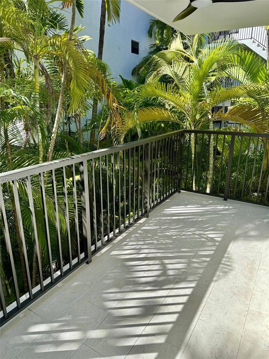 101 Ocean Lane Drive, #205, Key Biscayne, Key Biscayne, FL 33149 Covered balcony featuring tile flooring, dark metal railing, and an overhead ceiling fan, set against mature palm trees