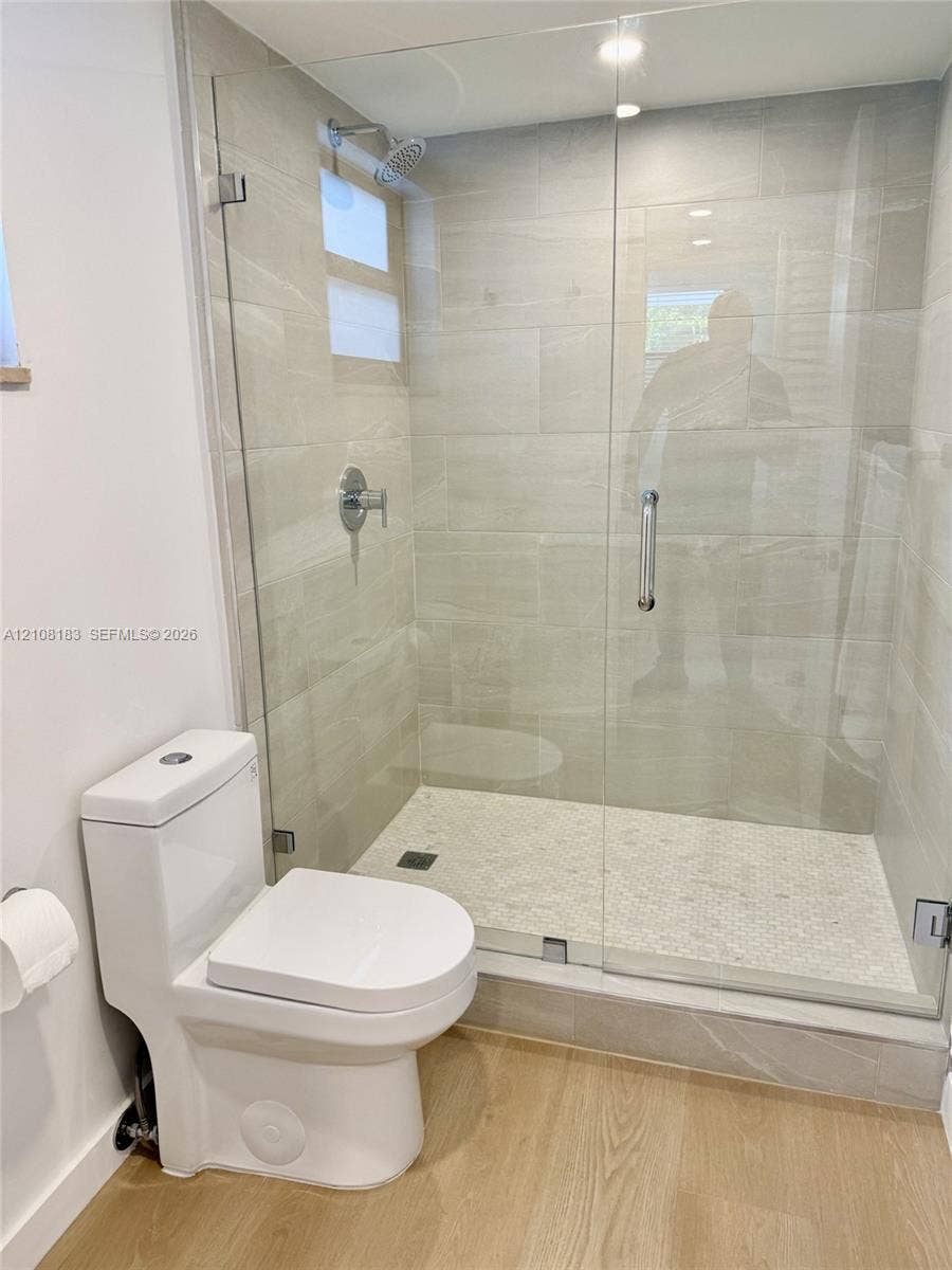 101 Ocean Lane Drive, #205, Key Biscayne, Key Biscayne, FL 33149 Walk-in shower featuring a glass enclosure, light-toned wall tile, pebble-textured flooring, and a chrome rainfall showerhead, complemented by a dual-flush toilet and wood-finish flooring