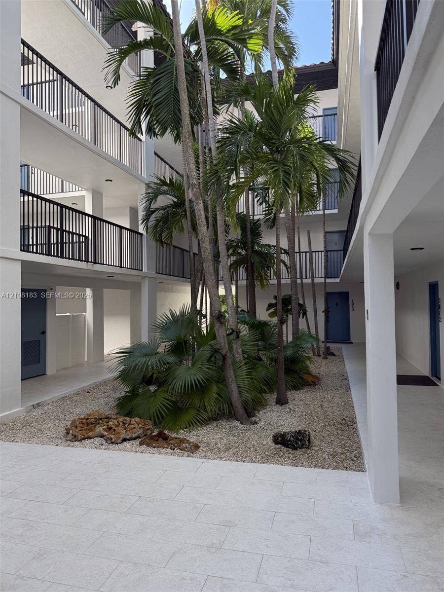 101 Ocean Lane Drive, #205, Key Biscayne, Key Biscayne, FL 33149 Central courtyard featuring stone-paved walkways, mature palm trees, decorative rock landscaping, and multi-level balconies with black metal railings