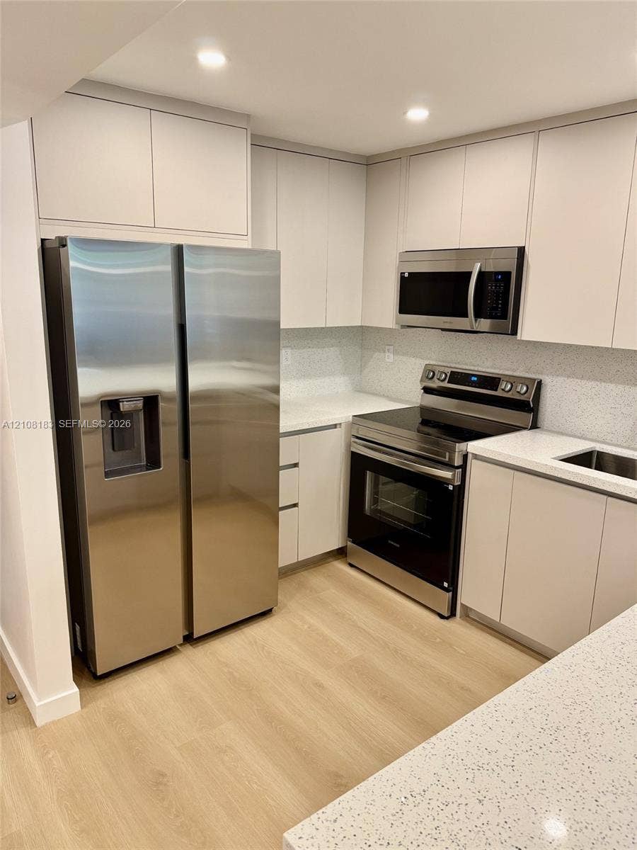 101 Ocean Lane Drive, #205, Key Biscayne, Key Biscayne, FL 33149 Kitchen featuring flat-panel cabinetry, light-toned countertops, wood-finish flooring, and stainless steel appliances including a side-by-side refrigerator, built-in microwave, and range