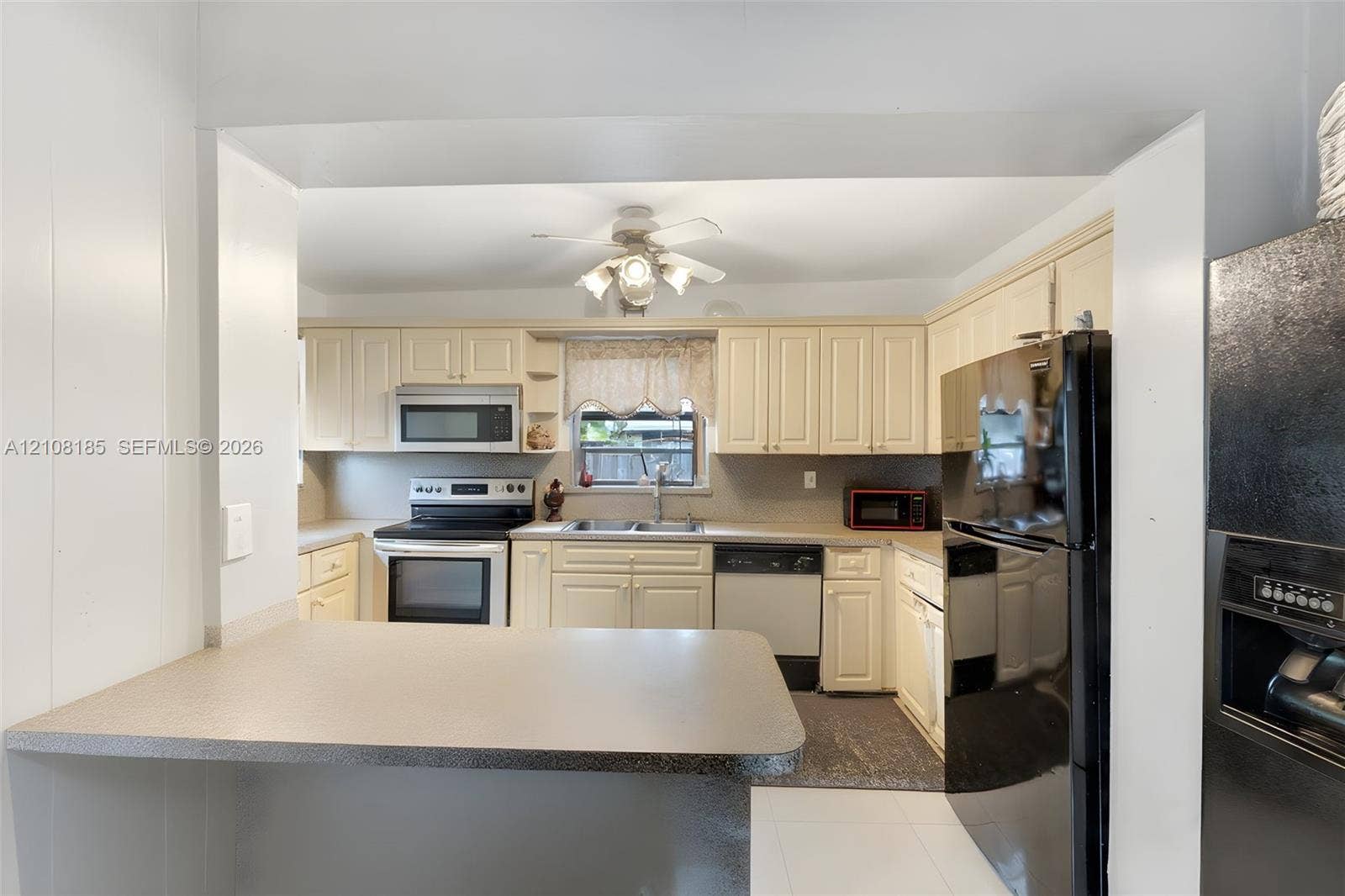 Kitchen featuring off-white cabinetry, solid-surface breakfast bar, black full-size refrigerator, integrated microwave, and built-in dishwasher
