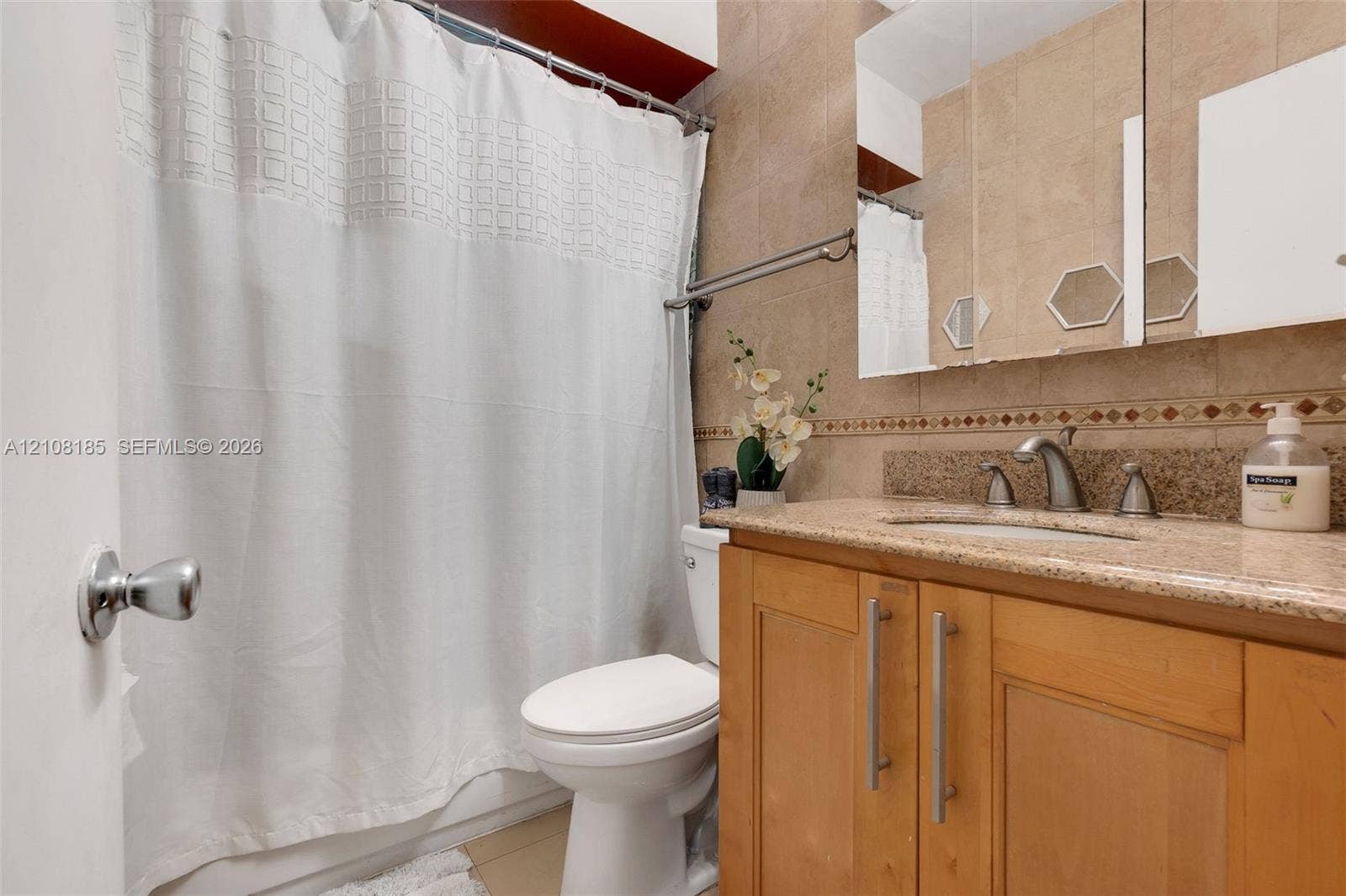 Bathroom featuring natural stone tile walls with decorative mosaic inlay, a wooden vanity cabinet with a stone countertop, an undermount sink with a metallic faucet, and a tri-fold mirrored medicine cabinet