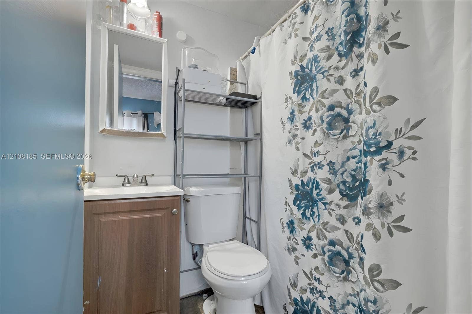 Bathroom featuring a vanity with a white basin, dual-handle faucet, and wall-mounted mirror, alongside a standard toilet and a shower-tub combination