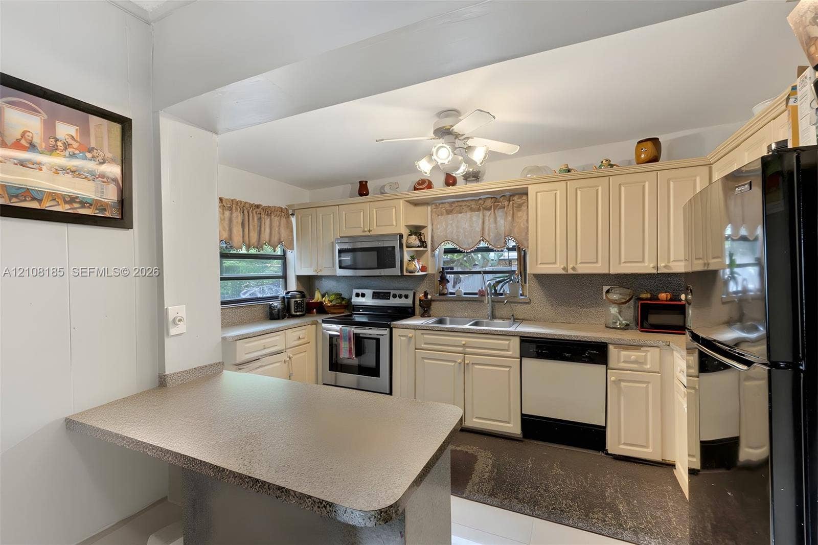 Kitchen featuring shaker-style cabinetry, an integrated breakfast bar, stainless steel appliances, a dual-basin sink, and a ceiling-mounted light fixture