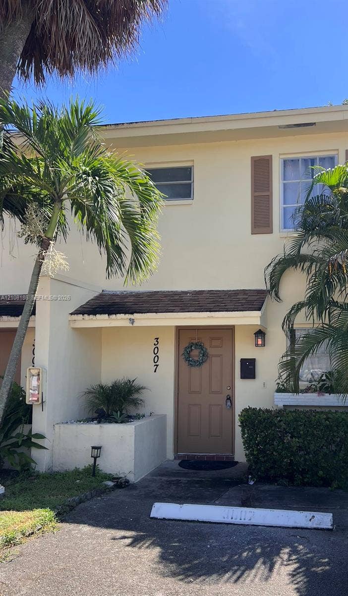 Two-story exterior featuring a stucco facade, covered entryway, panel-style door, shuttered windows, and a built-in masonry planter