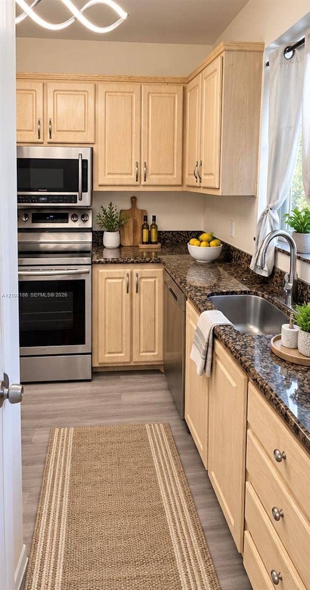 Kitchen featuring light wood cabinetry, stone countertops, stainless steel appliances, stainless steel undermount sink, and wood-finish flooring