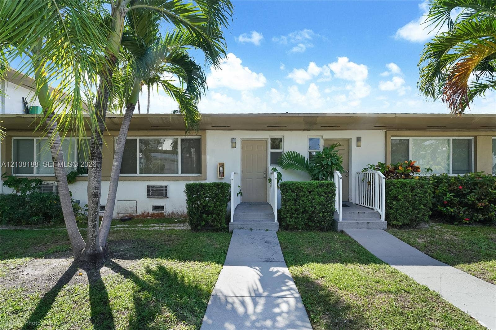 9790 E Bay Harbor Drive, #3N, Bay Harbor Islands, Bay Harbor Islands, FL 33154 Single-story exterior featuring a light-toned stucco facade, dual entry points with concrete steps, metal handrails, and mature palm trees