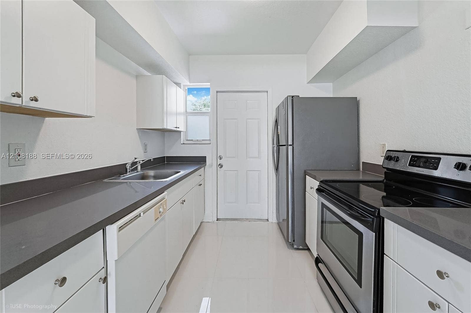 9790 E Bay Harbor Drive, #3N, Bay Harbor Islands, Bay Harbor Islands, FL 33154 Galley kitchen featuring white shaker-style cabinetry, solid-surface countertops, stainless steel appliances, a recessed stainless steel sink with a pull-out faucet, and tile flooring